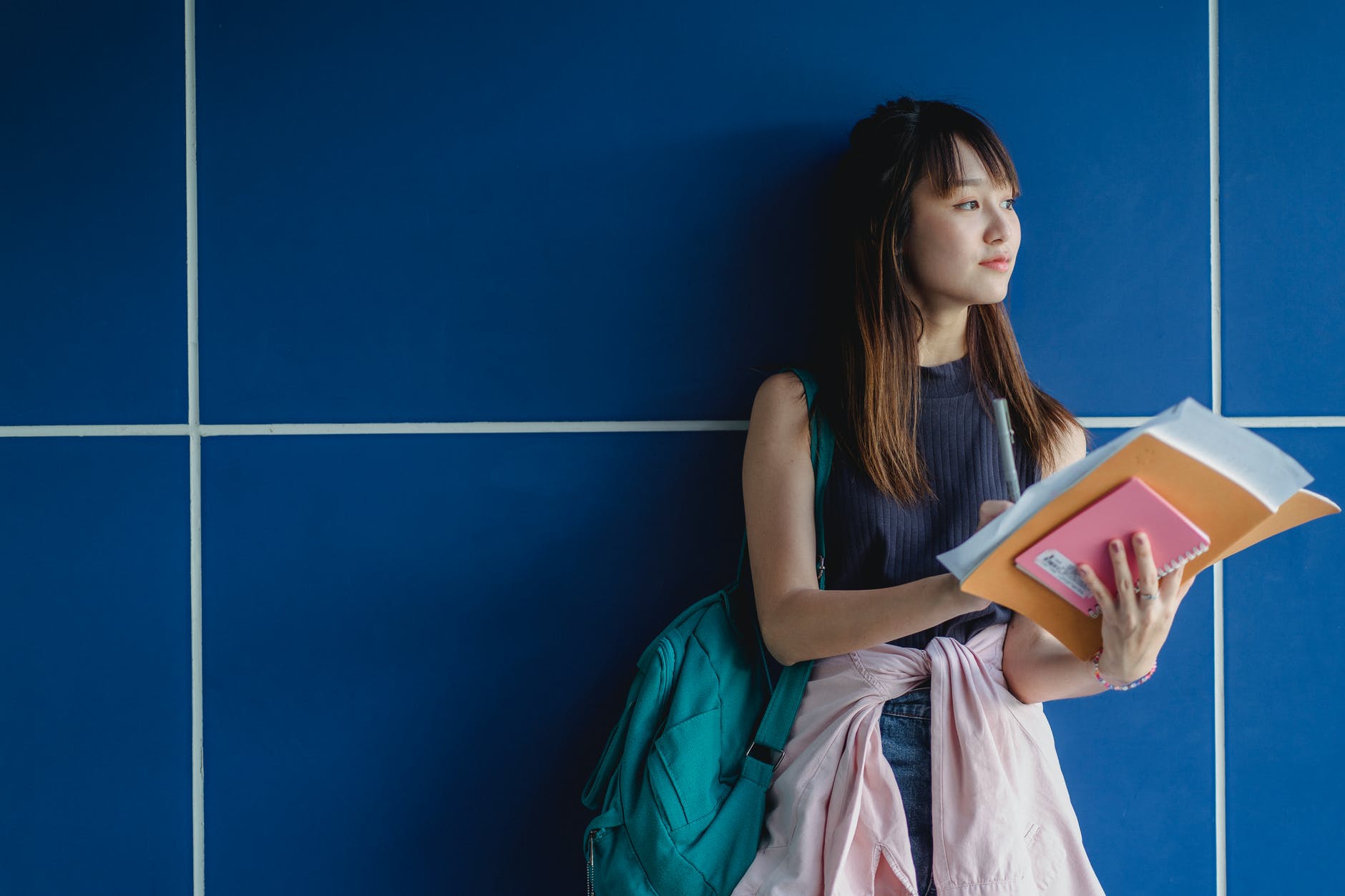 contemplative asian student with copybooks near tiled wall