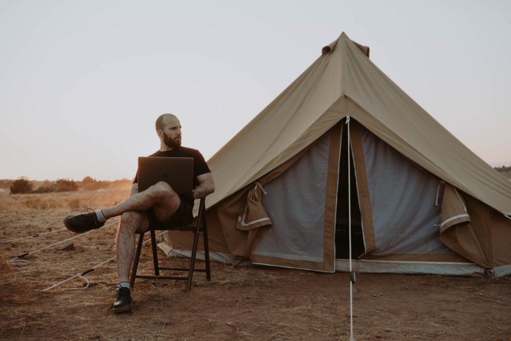 man relaxing with laptop near tent